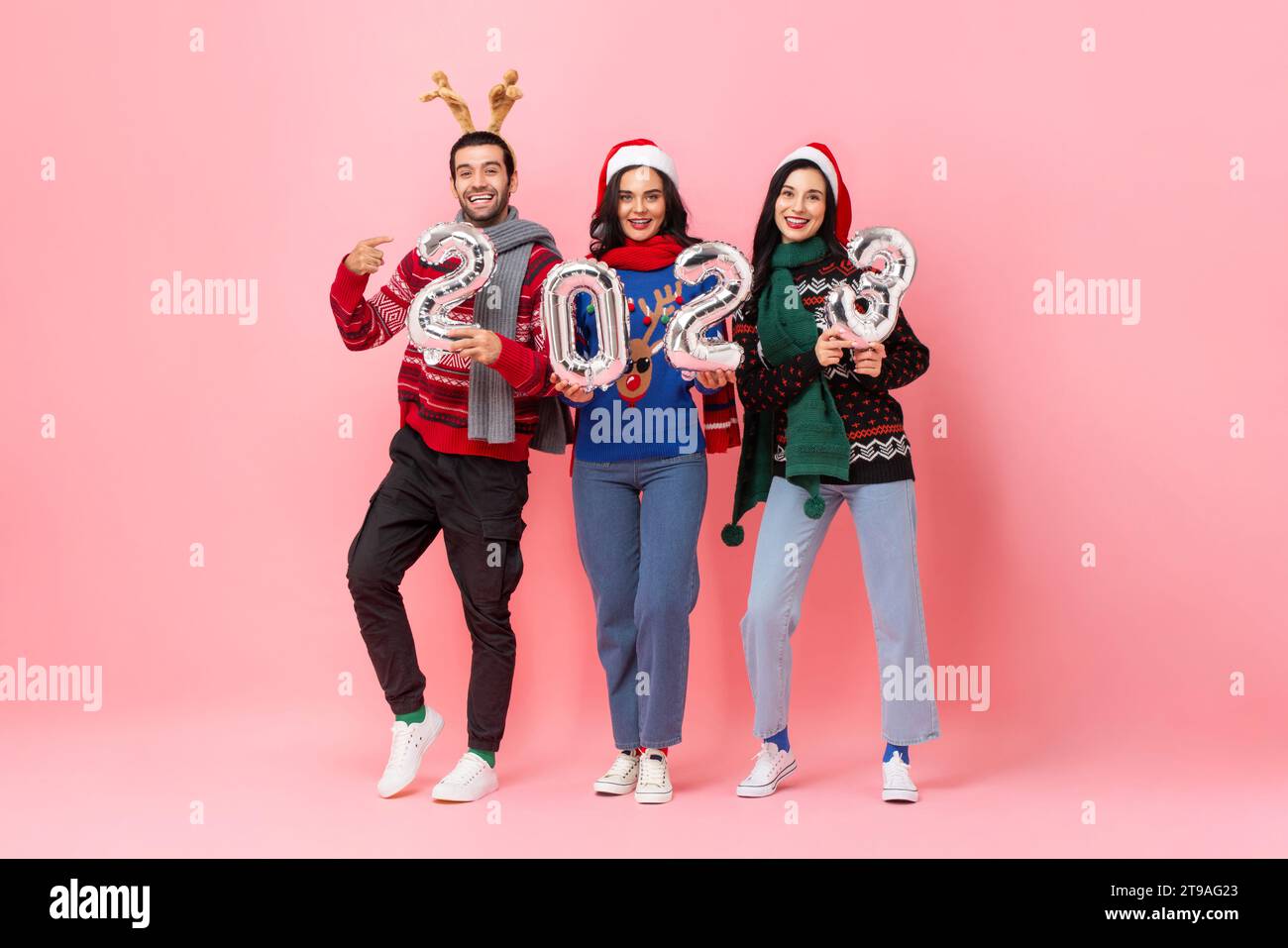 Studio drehte ein Porträt in voller Länge Weihnachten 2023, Gruppe glücklicher männlicher und weiblicher Freunde, die Pullover in isoliertem rosa Hintergrund trugen Stockfoto