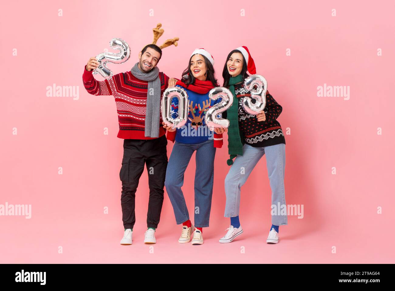 Studio drehte Ganzkörperporträt Weihnachten 2023, Gruppe glücklicher männlicher und weiblicher Freunde, die Pullover in isoliertem rosa Hintergrund trugen Stockfoto