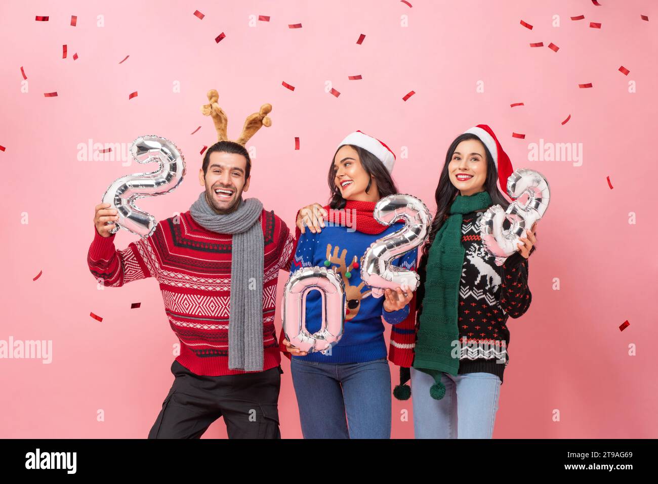 Gruppe glücklicher männlicher und weiblicher Freunde, die Pullover tragen, um Weihnachten 2023 zu feiern, im Studio Porträt in rosa Hintergrund aufgenommen Stockfoto