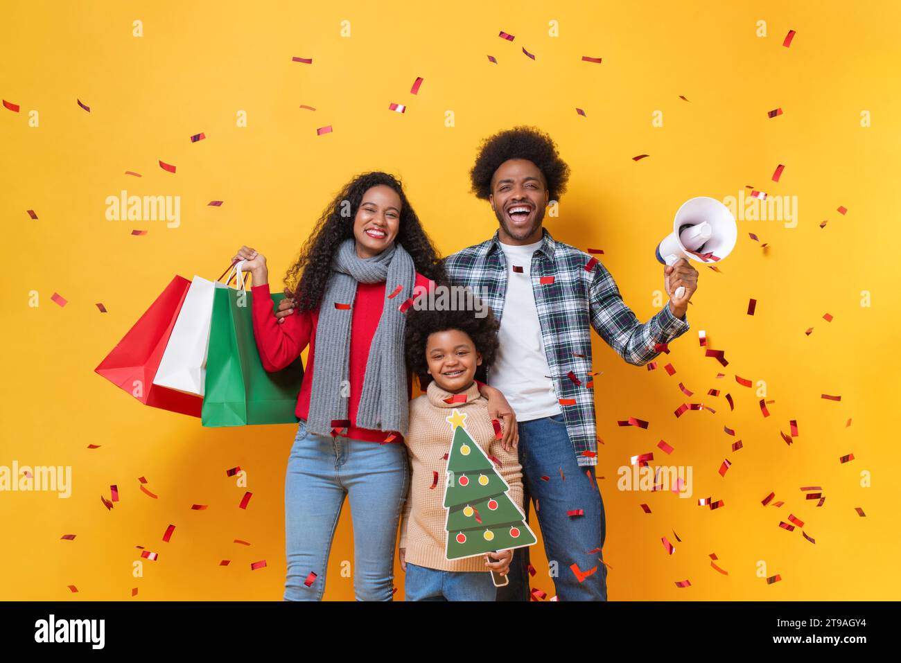 Glückliche afroamerikanische Familie im festlichen Weihnachtsfeierstudio geschossen gelben Farbhintergrund mit Konfetti Stockfoto