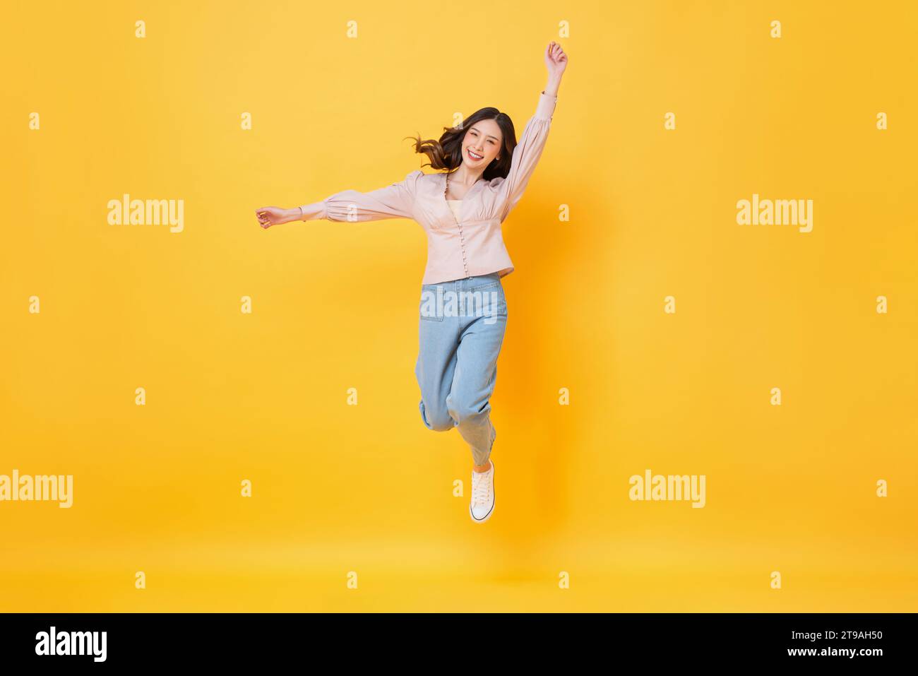Fröhliche asiatische Frau in lässiger Kleidung lächelnd und springend mit Händen nach oben in bunter gelber Farbe isolierte Hintergrundaufnahmen im Studio Stockfoto