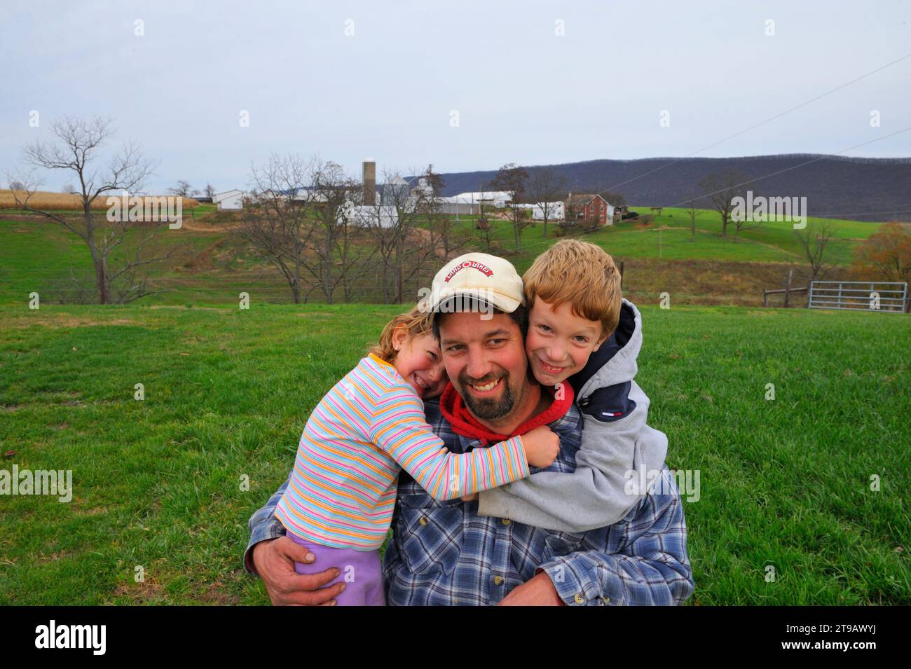 Ein Maisbauer posiert für ein Porträt mit seinen beiden lächelnden Kindern auf einem riesigen grünen Feld auf seiner Farm in Bloomsburg, PA. Stockfoto