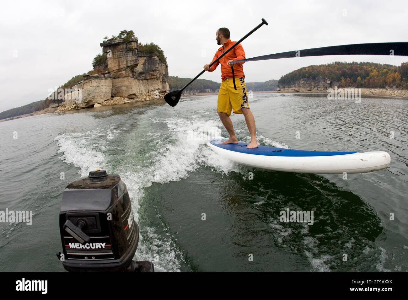 Ein Mann steht auf dem Paddleboarder, der von einem kleinen Boot gezogen wird. Stockfoto