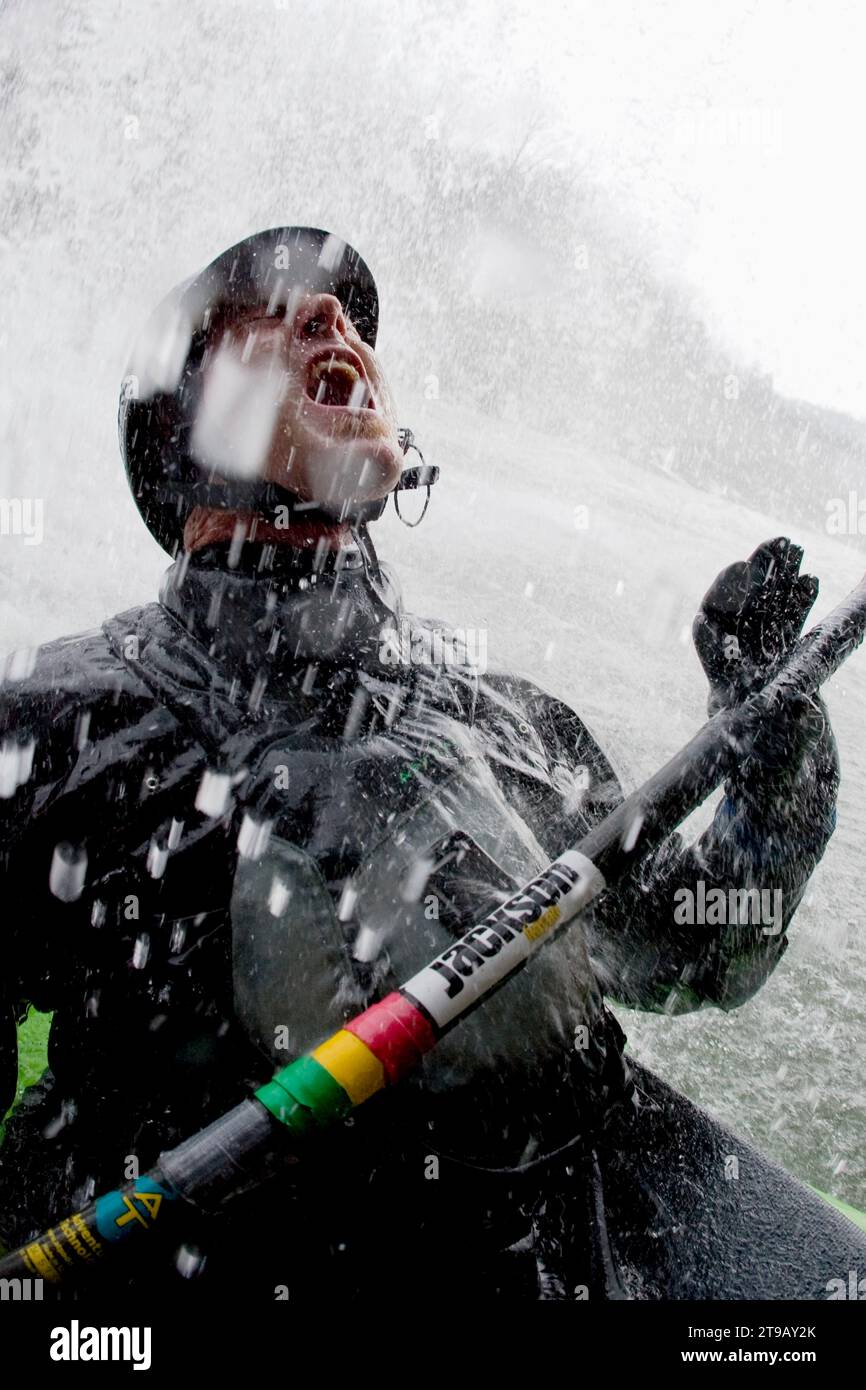 Männlicher Kajakfahrer, der in einen Wasserfall blickt, während er auf ihn spritzt. Stockfoto