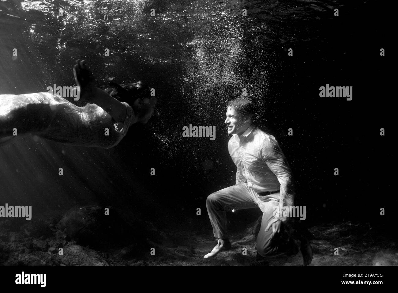 Schwarz-weiß-Unterwasserbild eines Mannes und einer Frau, die in ihrer Hochzeitskleidung in einer Cenote schwimmen. Stockfoto