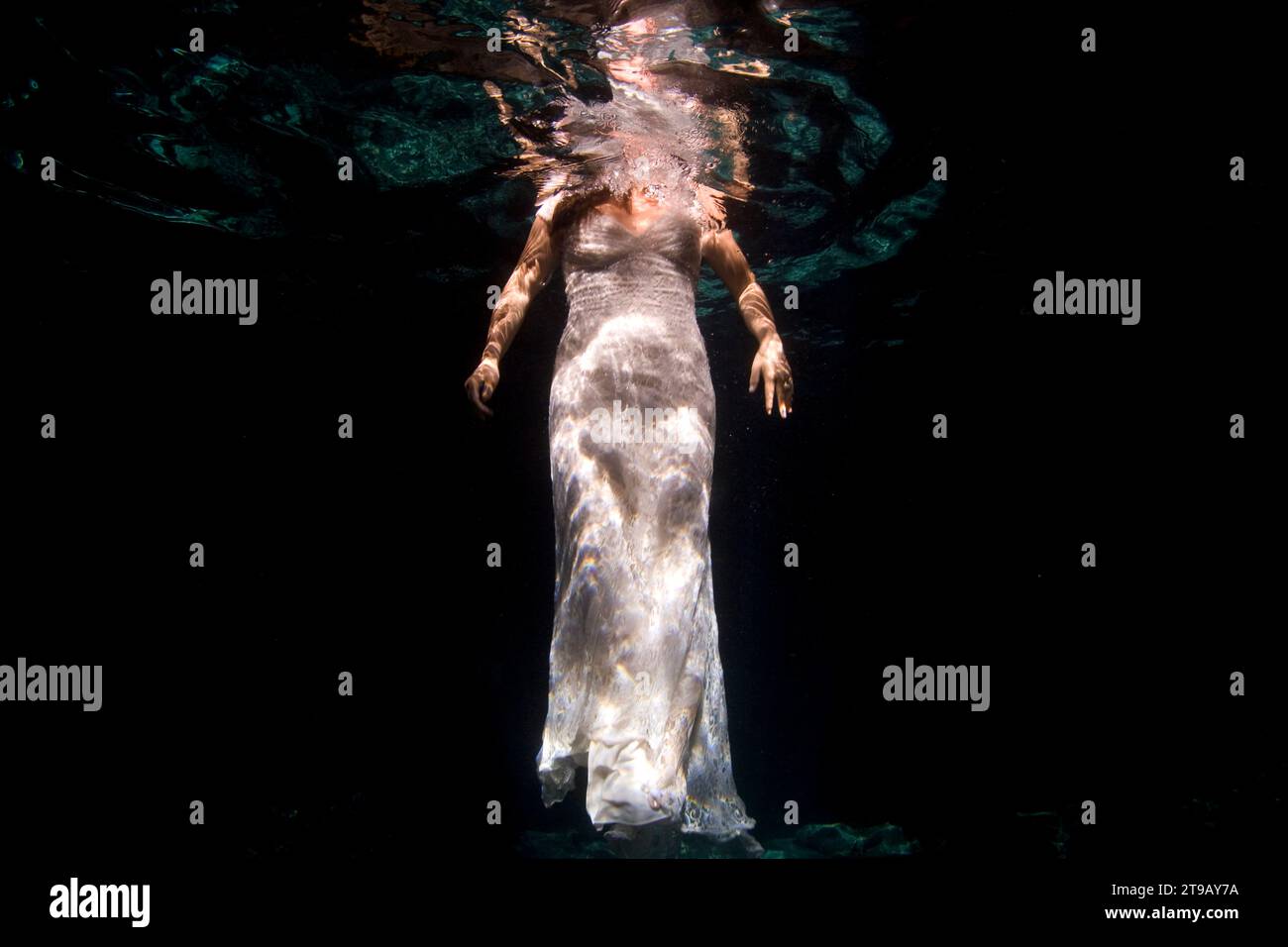 Unterwasserbild eines Mannes und einer Frau, die in ihrer Hochzeitskleidung in einer Cenote schwimmen. Stockfoto