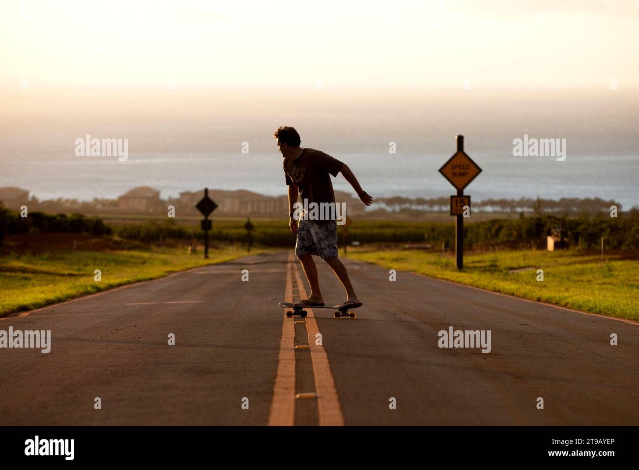 Die Perspektive eines Mannes Longboard-Skateboarden in schönem Licht einen Hügel hinunter mit dem Ozean im Hintergrund. Stockfoto