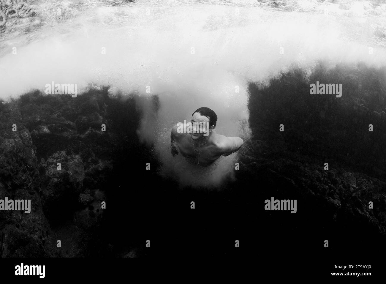 Ein Mann lächelt und schwimmt unter Wasser, nachdem er von einer Klippe gesprungen ist. Stockfoto