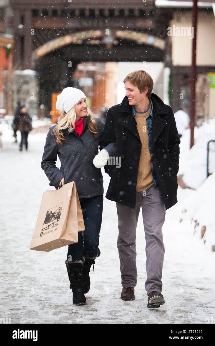 Junge attraktive Paare, die in einem Dorf mit Schneefall einkaufen. Stockfoto