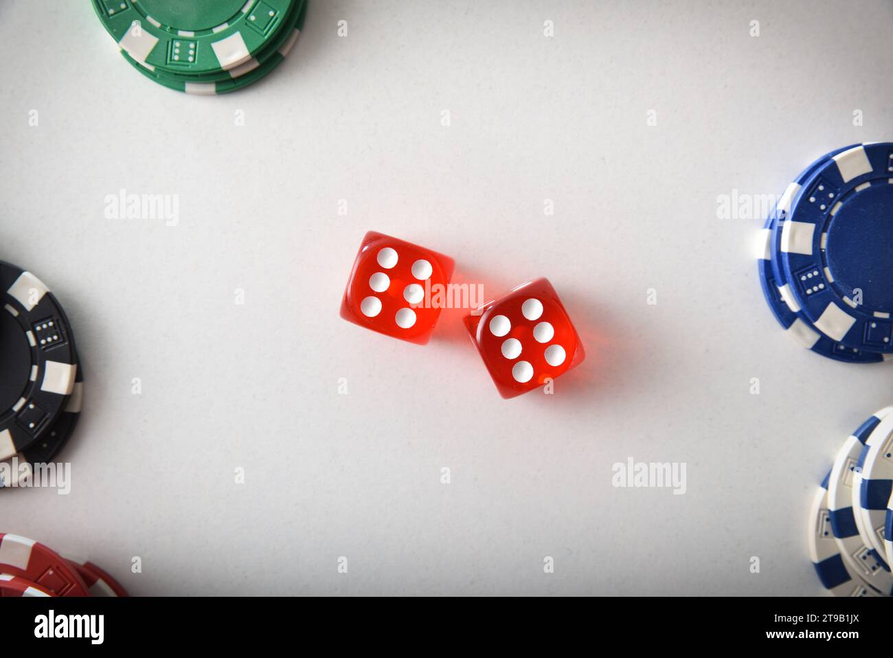 Spielhintergrund mit zwei roten Würfeln in der Mitte und einem Stapel von verschiedenfarbigen Wett-Chips an den Enden isoliert auf weißem Tisch. Draufsicht Stockfoto