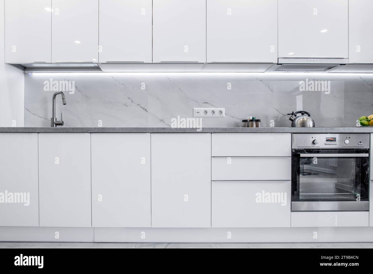 Eine saubere, helle Küche mit reinweißen Schränken und modernem Design. Das Ambiente der Küche ist einfach, erfrischend und einladend Stockfoto