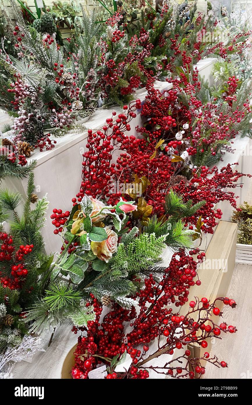 Künstliche Weihnachtsbeeren zur Dekoration, die zum Verkauf im Supermarkt zubereitet werden. Vielfalt an farbenfrohen Dekorationen auf Holzregalen eines großen Ladens. Stockfoto