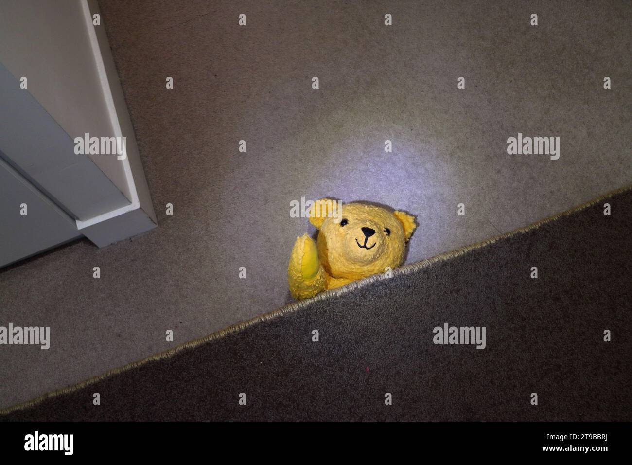 Gelbe Teddybär-Spielzeugpuppe versteckt und winkt unter einem Teppich Stockfoto