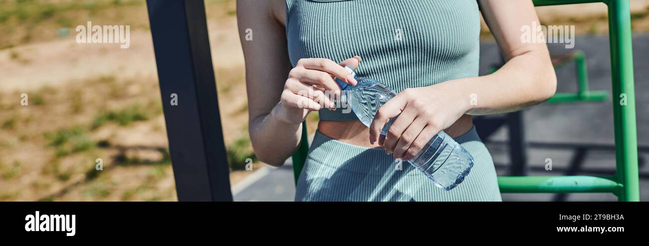 Beschnittenes Banner einer Frau in Radshorts und Crop Top, das Flaschenwasser in der Nähe einer vertikalen Leiter hält Stockfoto