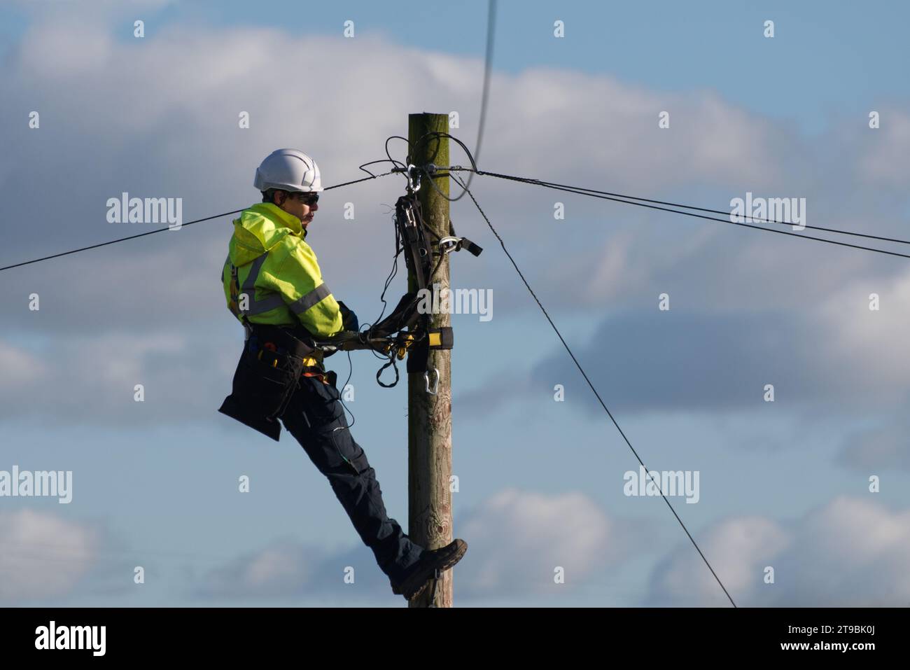 Ein männlicher Telekommunikationsingenieur repariert ein Telefonkabel an der Spitze eines Telefon-/Telegrafenmasts in einem ländlichen Dorf, Großbritannien, ein Arbeiter mit offenem Zugriff Stockfoto