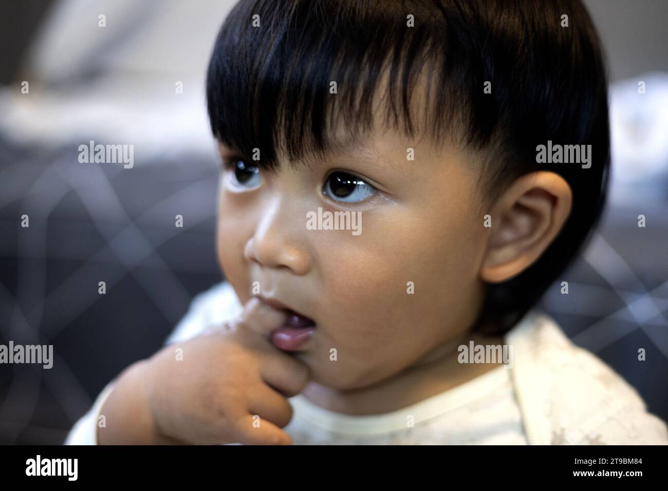 Schließen Sie den asiatischen Jungen, der Finger in den Mund lutscht. Entzückender kleiner asiatischer Junge, der Finger im Mund lutscht. Stockfoto