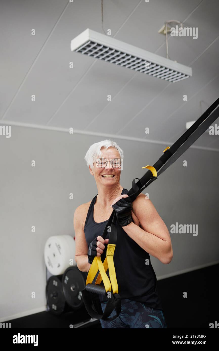 Lächelnde Seniorin, die im Fitnessstudio steht und in die Kamera blickt Stockfoto