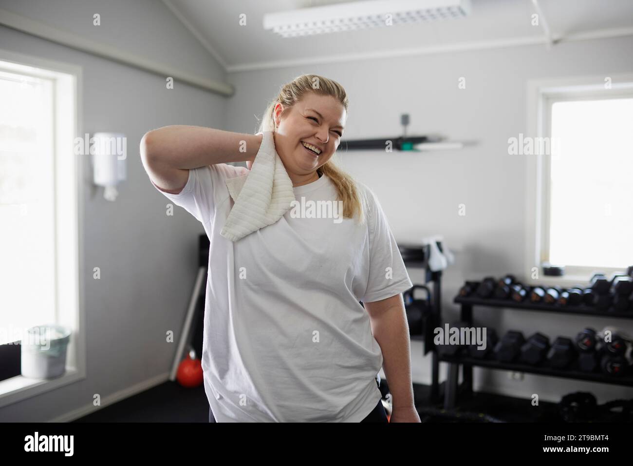 Glückliche Frau trocknet den Hals mit Handtuch im Fitnessstudio Stockfoto