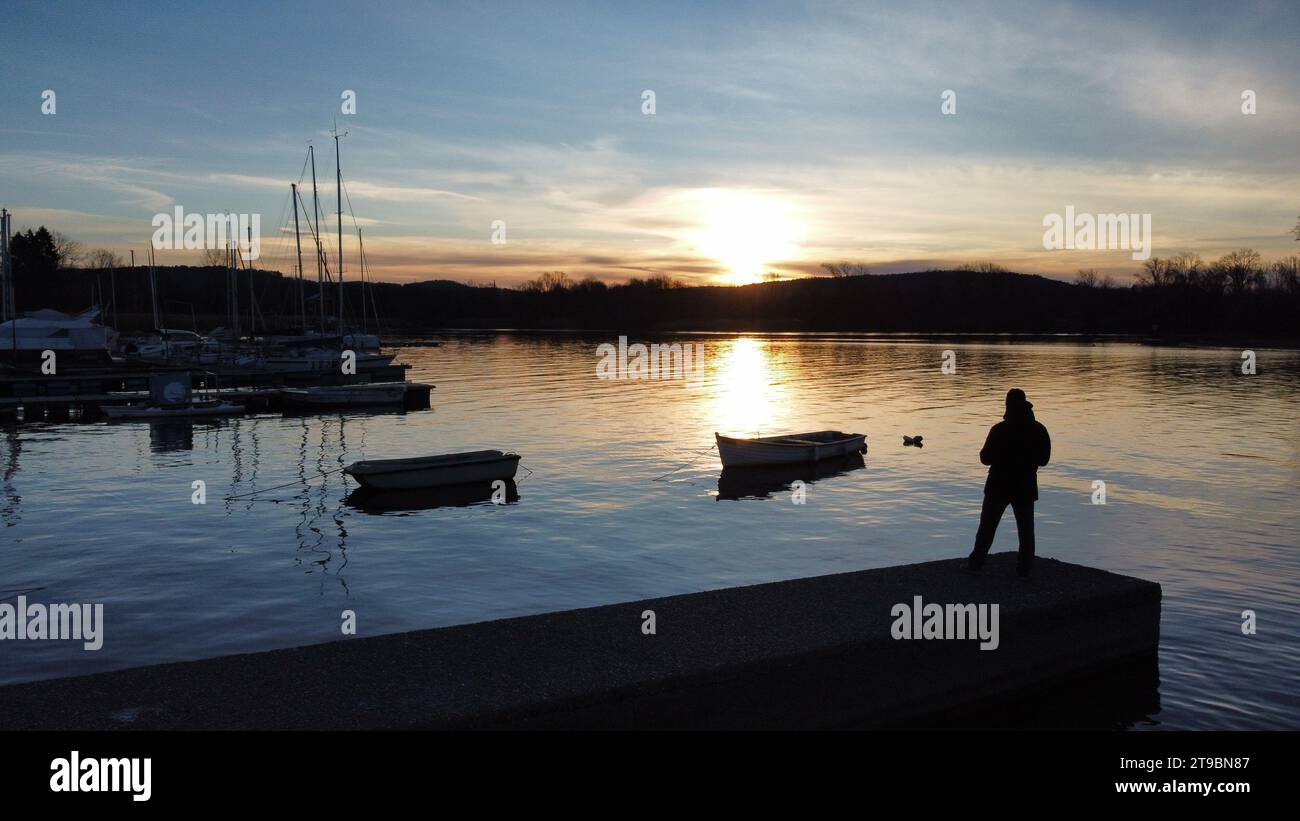 Boote und Docks bei Sonnenaufgang spiegeln sich am Lago Maggiore in Italien. Farbtöne im Schatten der Nacht Stockfoto