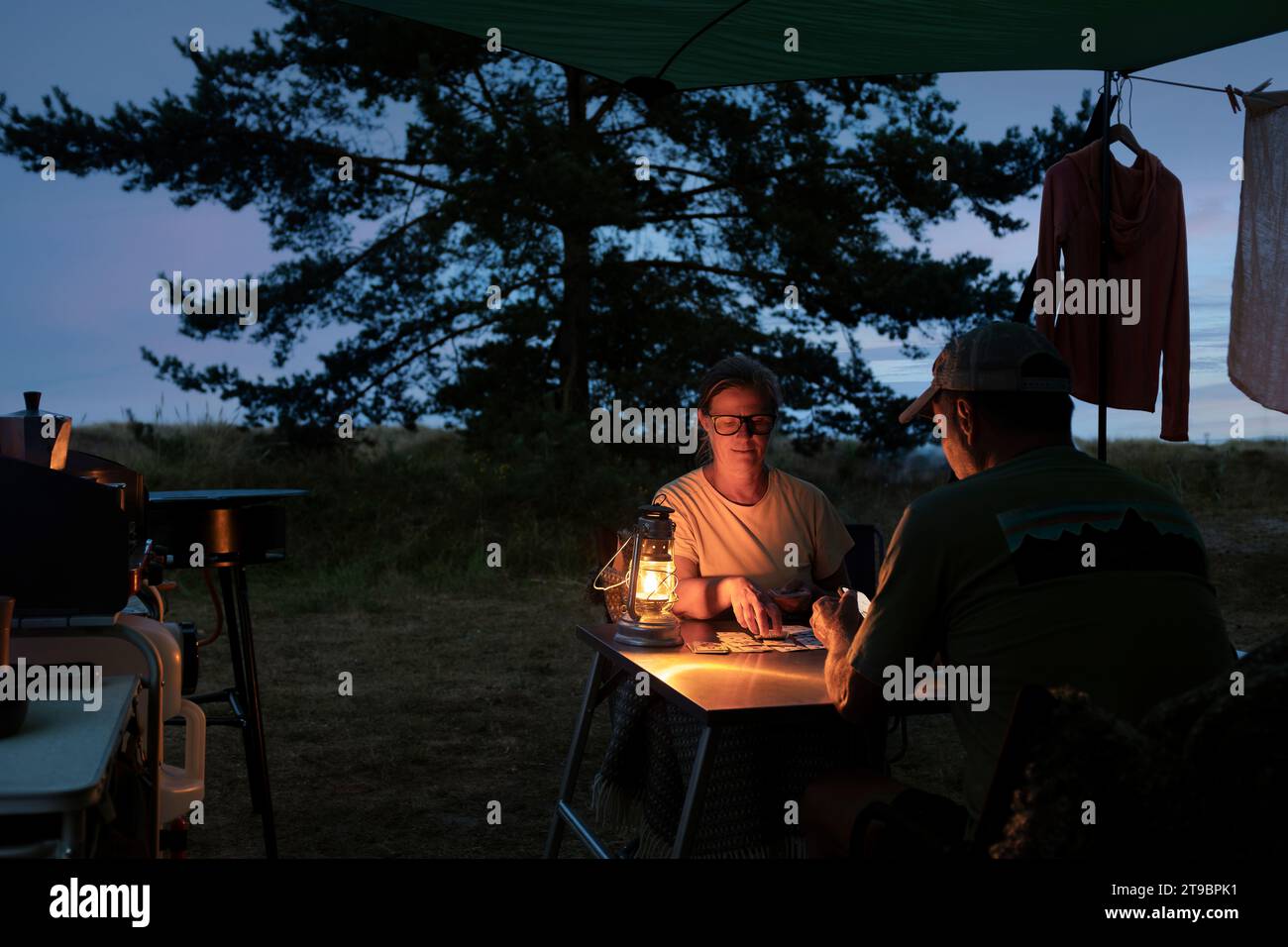 Ein paar, die Karten spielen, während sie in der Abenddämmerung campen Stockfoto