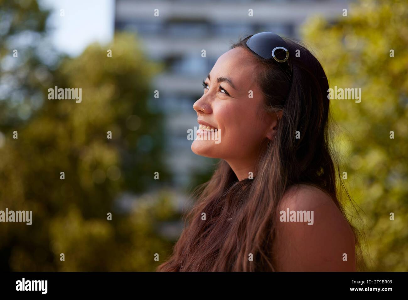 Lächelnde junge Frau, die draußen sitzt und wegschaut Stockfoto