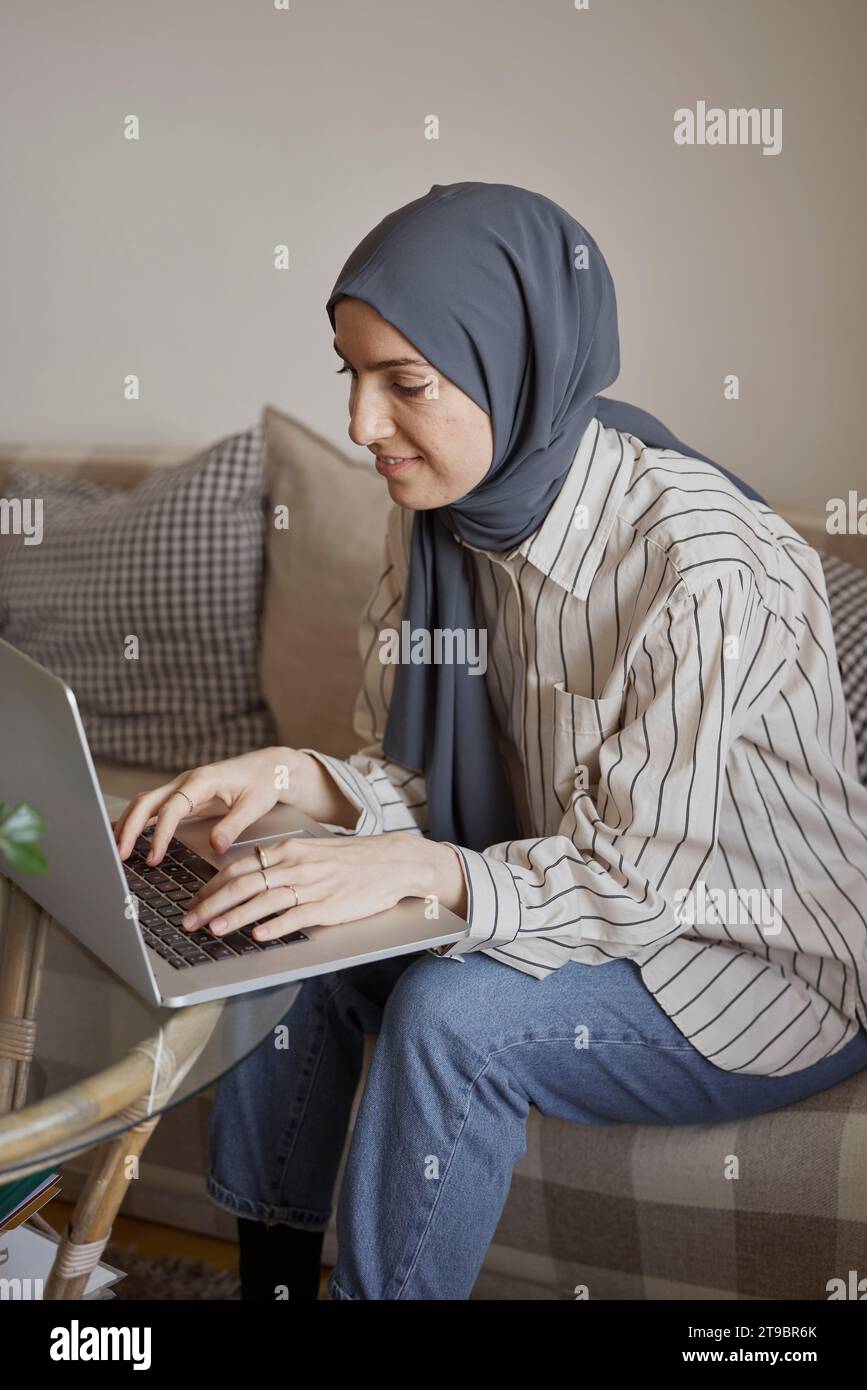 Junge Geschäftsfrau, die im Wohnzimmer von zu Hause aus auf einem Laptop schreibt Stockfoto