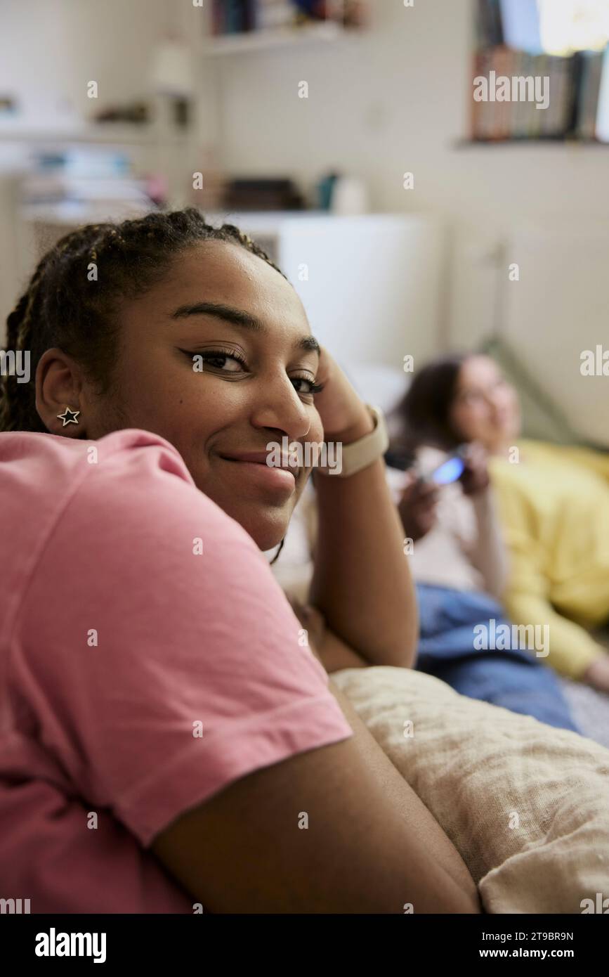 Lächelnder weiblicher Teenager mit Freunden im Hintergrund zu Hause Stockfoto