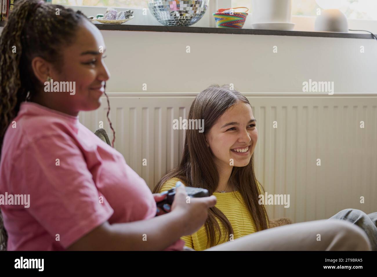 Lächelnder weiblicher Teenager, der ein Videospiel von einem Freund zu Hause spielt Stockfoto