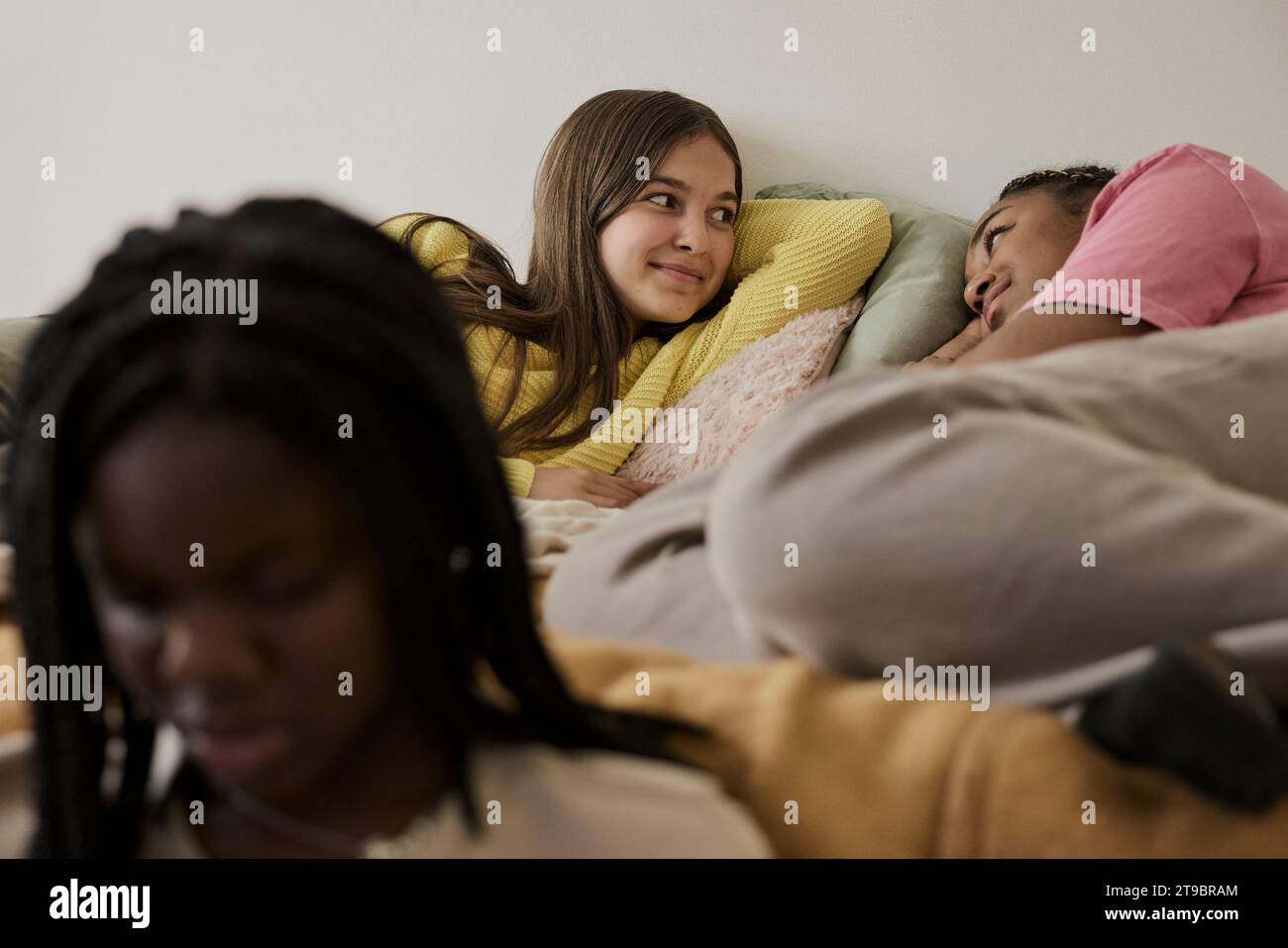 Mädchen im Teenageralter, die im Bett liegen, mit einer Freundin, die zu Hause vor sich sitzt Stockfoto