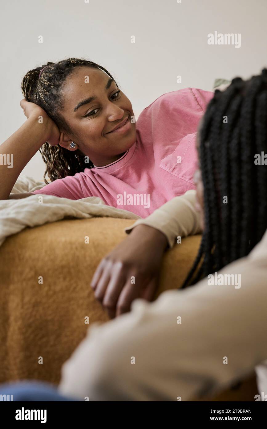 Lächelndes Teenager-Mädchen, das auf dem Bett liegt und mit einer Freundin im Schlafzimmer spricht Stockfoto