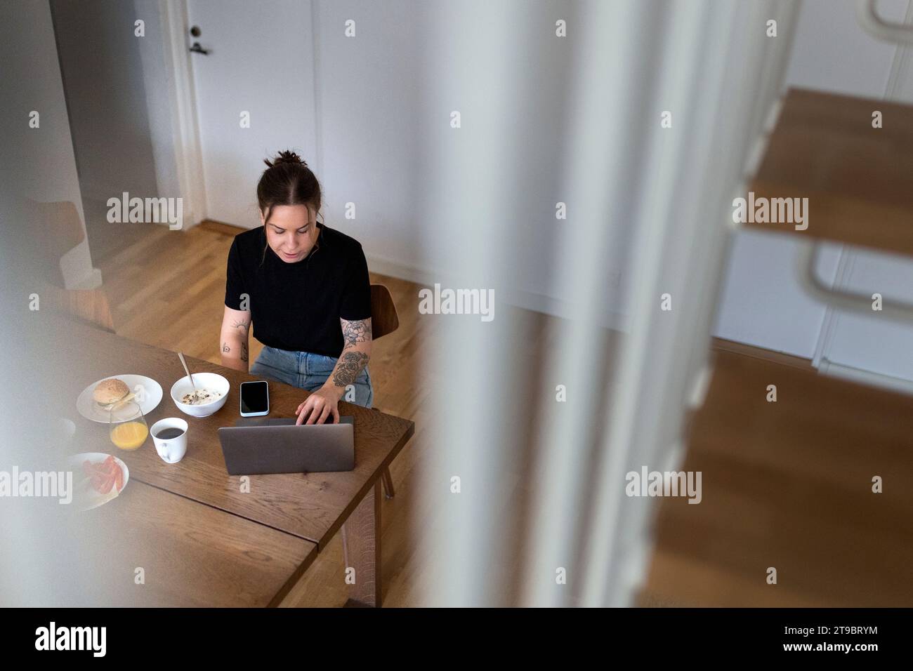 Hochwinkelansicht einer jungen Geschäftsfrau, die einen Laptop benutzt, während sie am Esstisch Telearbeit macht Stockfoto