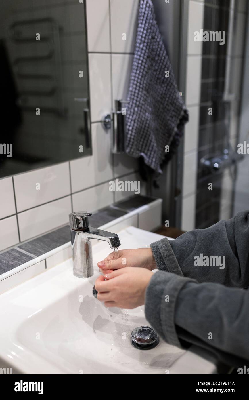 Abgeschnittene Hände einer Frau, die unter dem Wasserhahn im Waschbecken wäscht Stockfoto