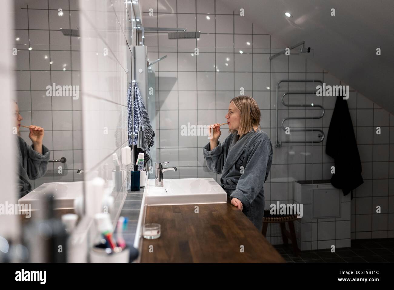 Seitenansicht der jungen blonden Frau, die im Bad Zähne putzt Stockfoto