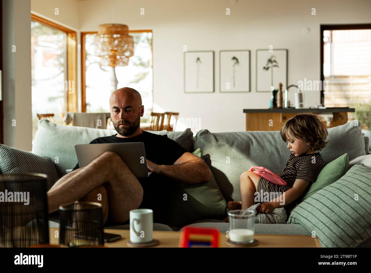 Reifer Mann, der mit seinem Sohn über einem Laptop arbeitet und ein digitales Tablet benutzt, das im Wohnzimmer auf dem Sofa sitzt Stockfoto