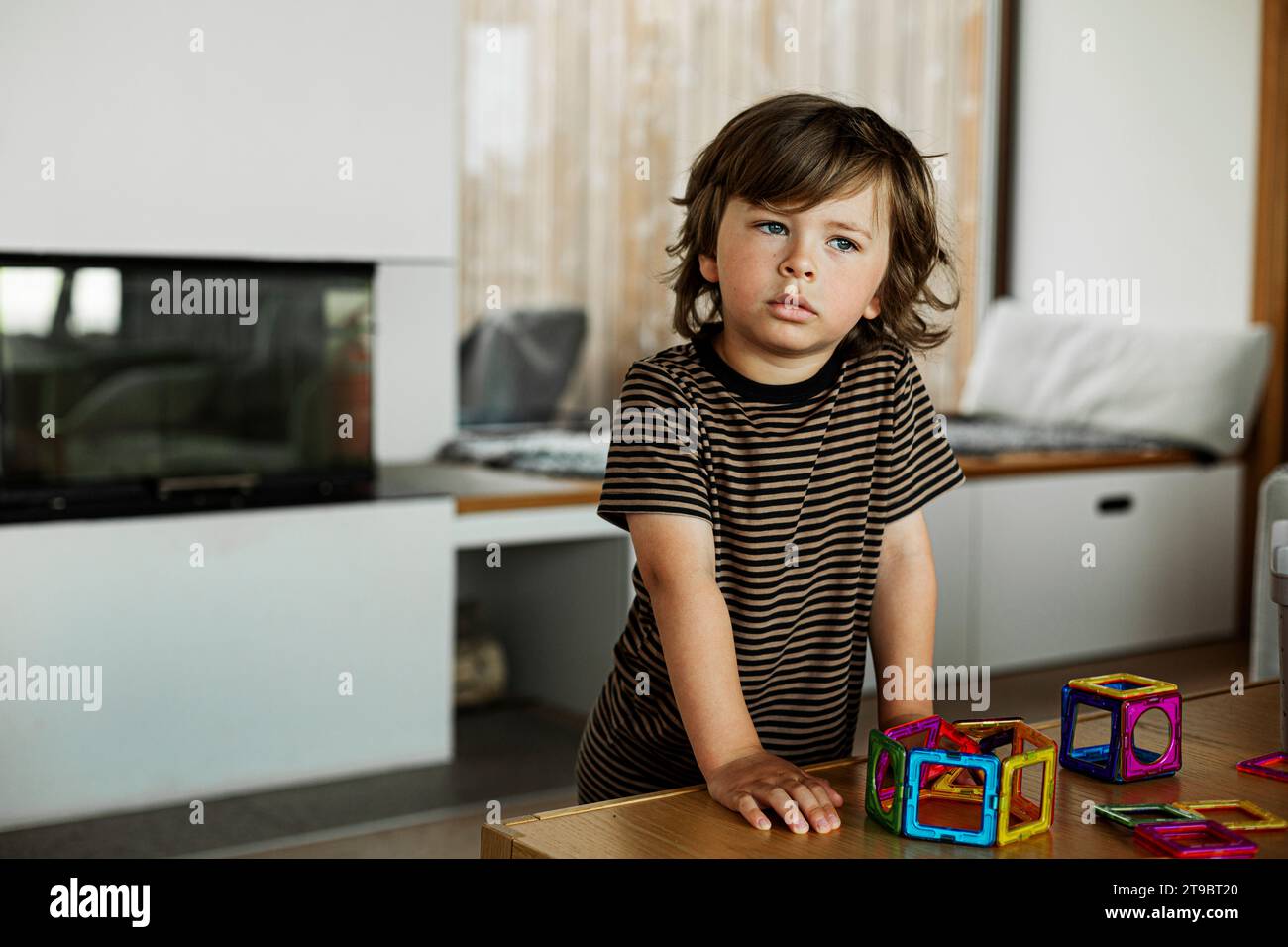 Besinnlicher Junge mit Spielzeugblock zu Hause auf dem Tisch Stockfoto