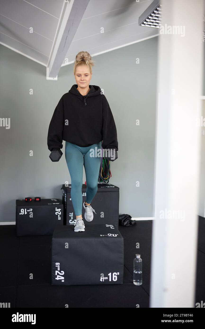 Volle Länge einer Frau, die auf Block mit Kurzhanteln im Health Club trainiert Stockfoto