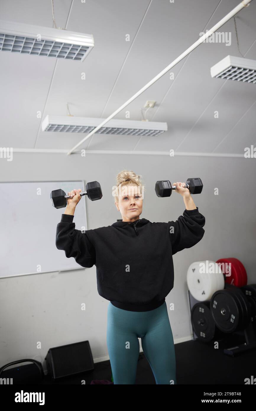 Frau, die mit Kurzhanteln im Fitnessclub trainiert Stockfoto