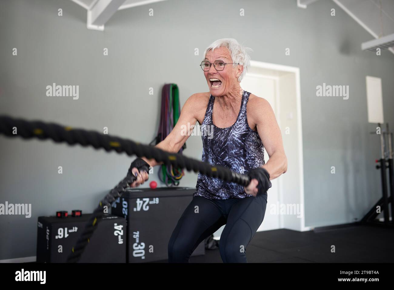 Aktive Seniorin schreiend beim Trainieren mit Seilen im Health Club Stockfoto