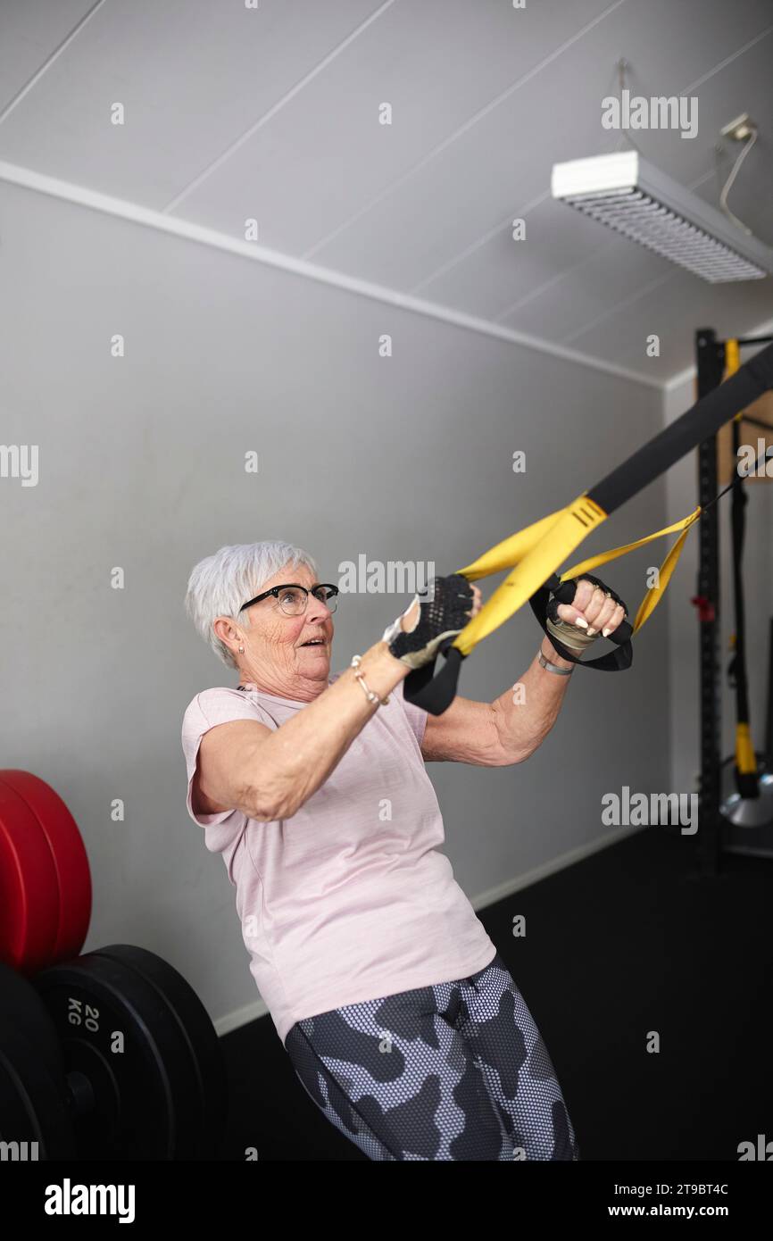 Aktive Seniorin, die auf Turnringen im Fitnessclub trainiert Stockfoto