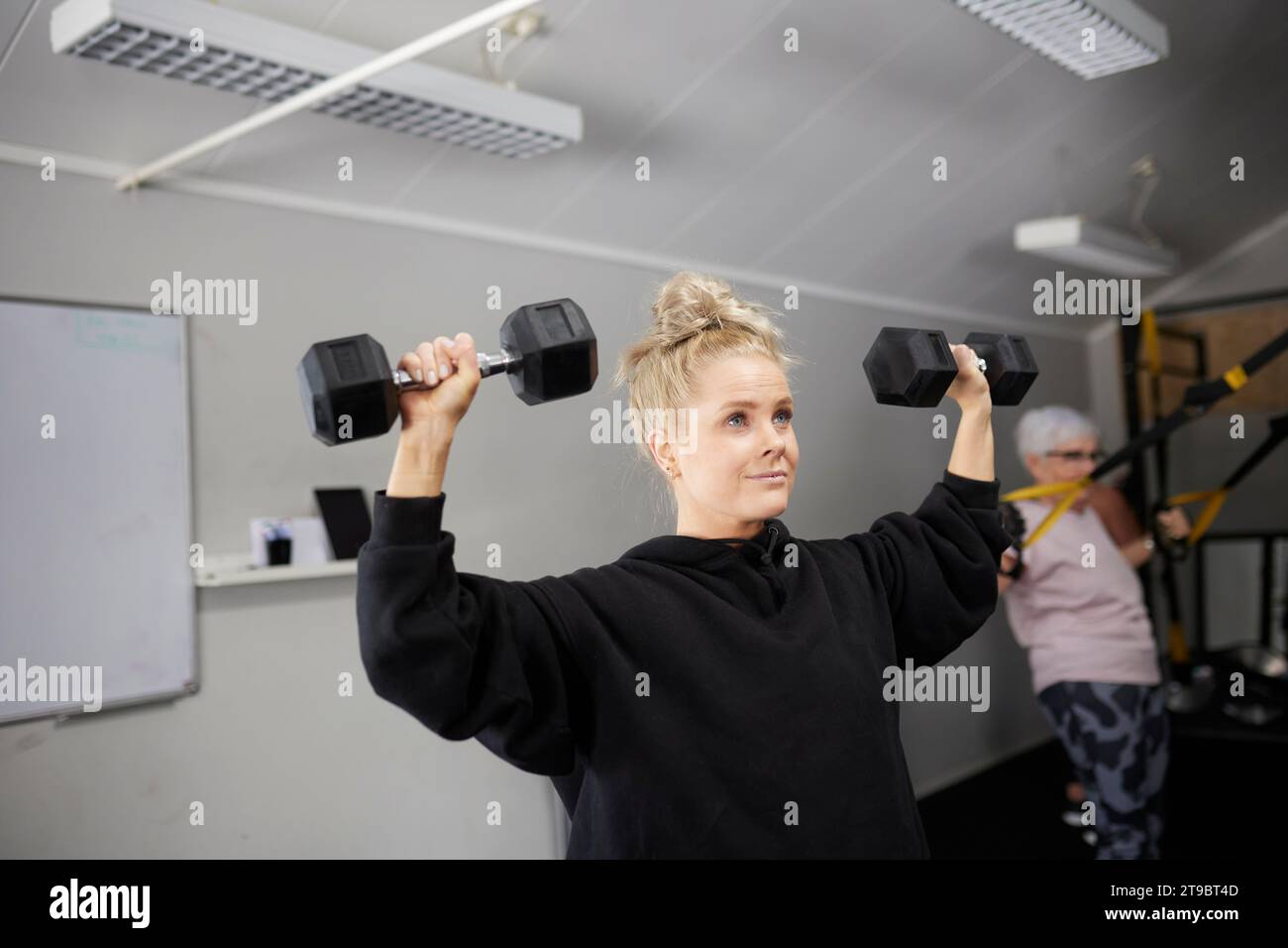 Blonde Frau, die mit Kurzhanteln im Fitnessclub trainiert Stockfoto