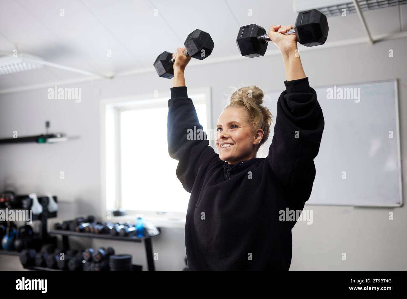 Lächelnde Frau, die mit Kurzhanteln im Fitnessclub trainiert Stockfoto