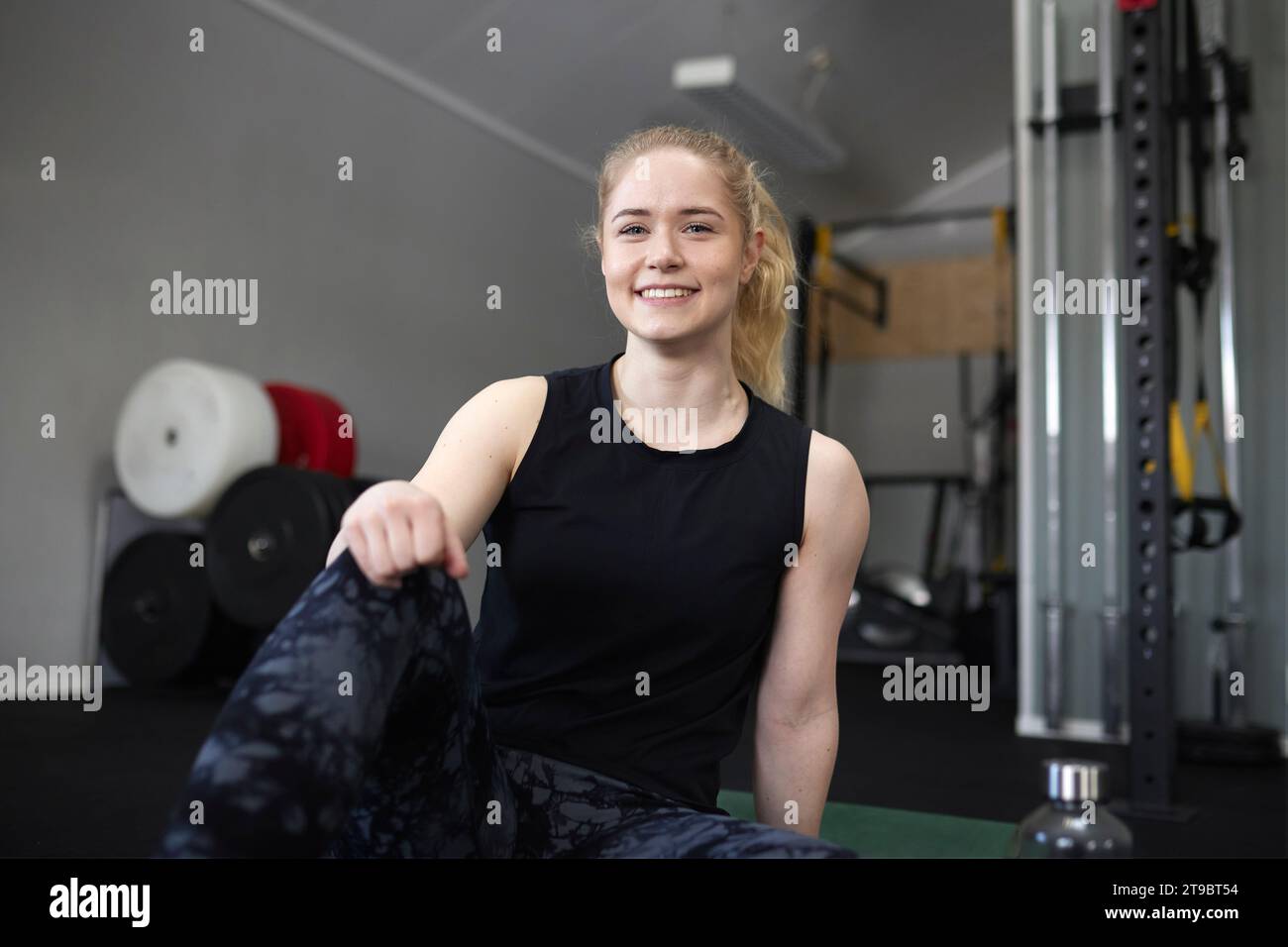 Porträt einer lächelnden jungen Frau, die im Fitnessstudio sitzt Stockfoto