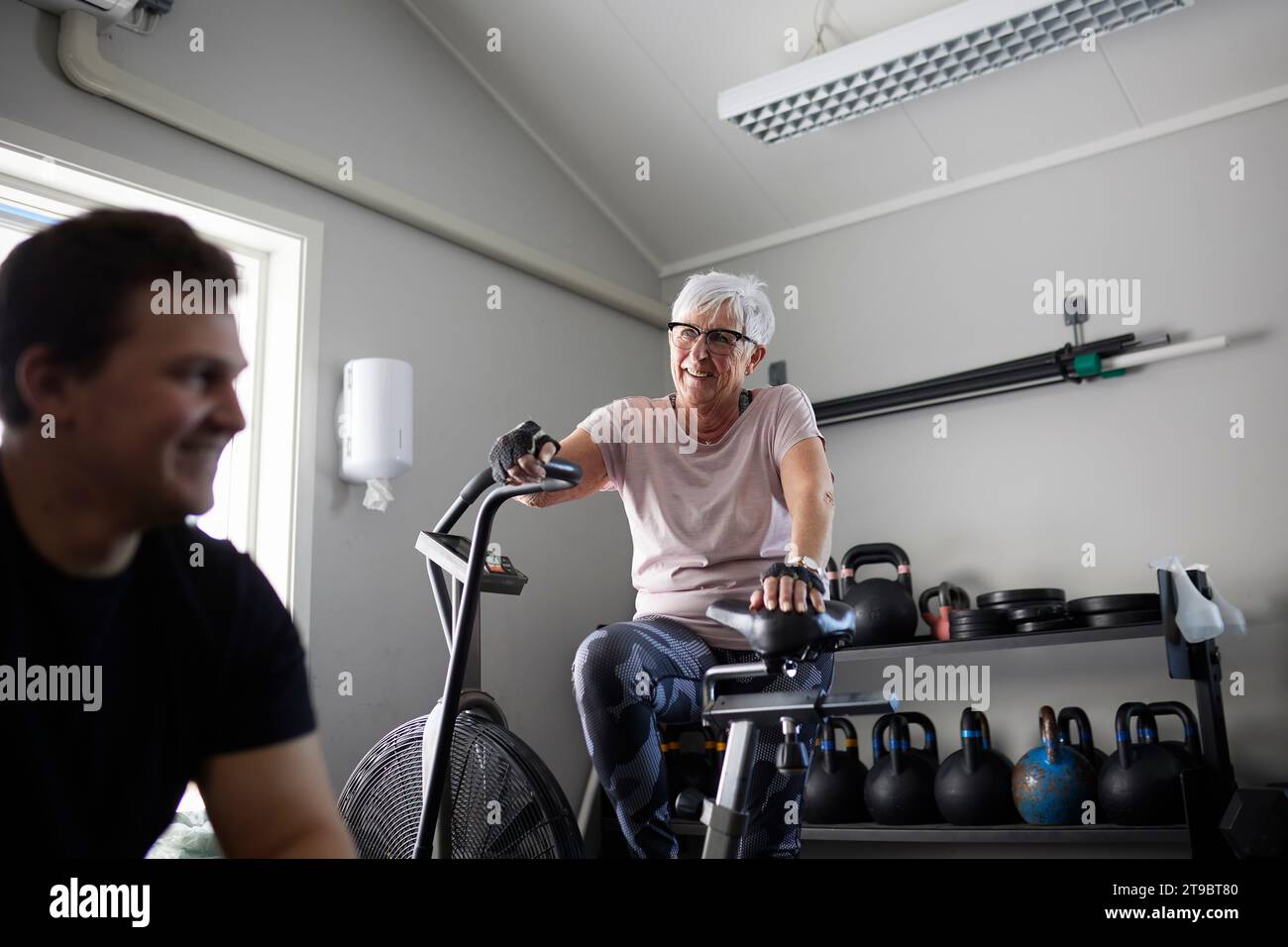 Tiefwinkelansicht einer lächelnden Seniorin mit dem Heimtrainer, die den Mann im Fitnessstudio ansieht Stockfoto