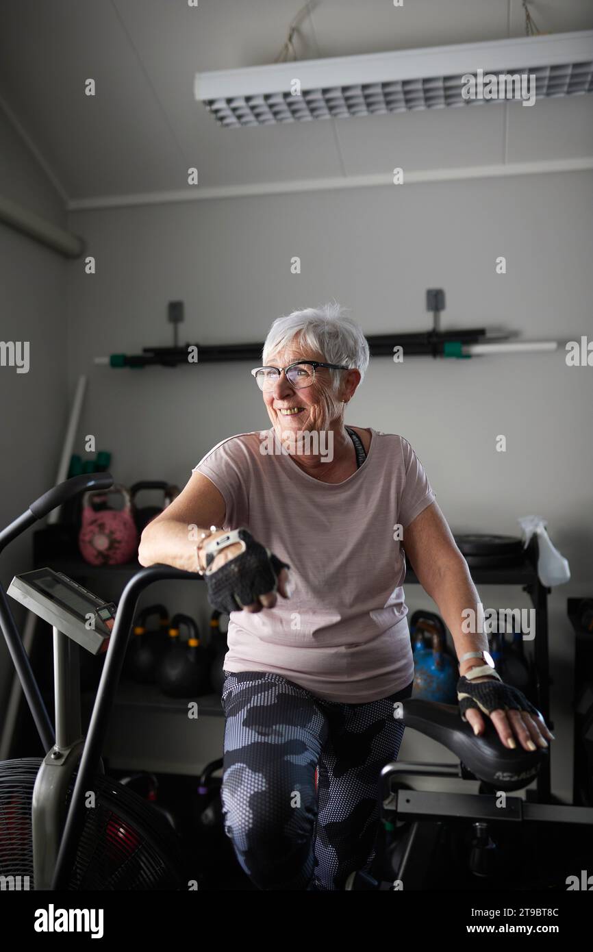 Glückliche Seniorin, die sich auf dem Heimtrainer im Health Club stützt Stockfoto