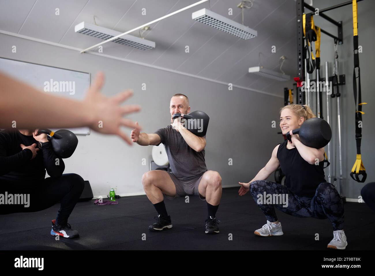 Männer und Frauen, die mit Kettlebells trainieren, während sie im Fitnessstudio hocken Stockfoto