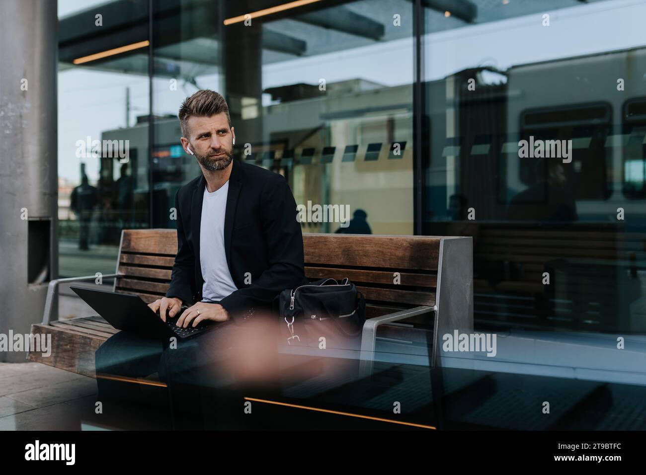 Selbstbewusster Geschäftsmann, der auf der Bank sitzt, während er am Bahnhof wartet Stockfoto