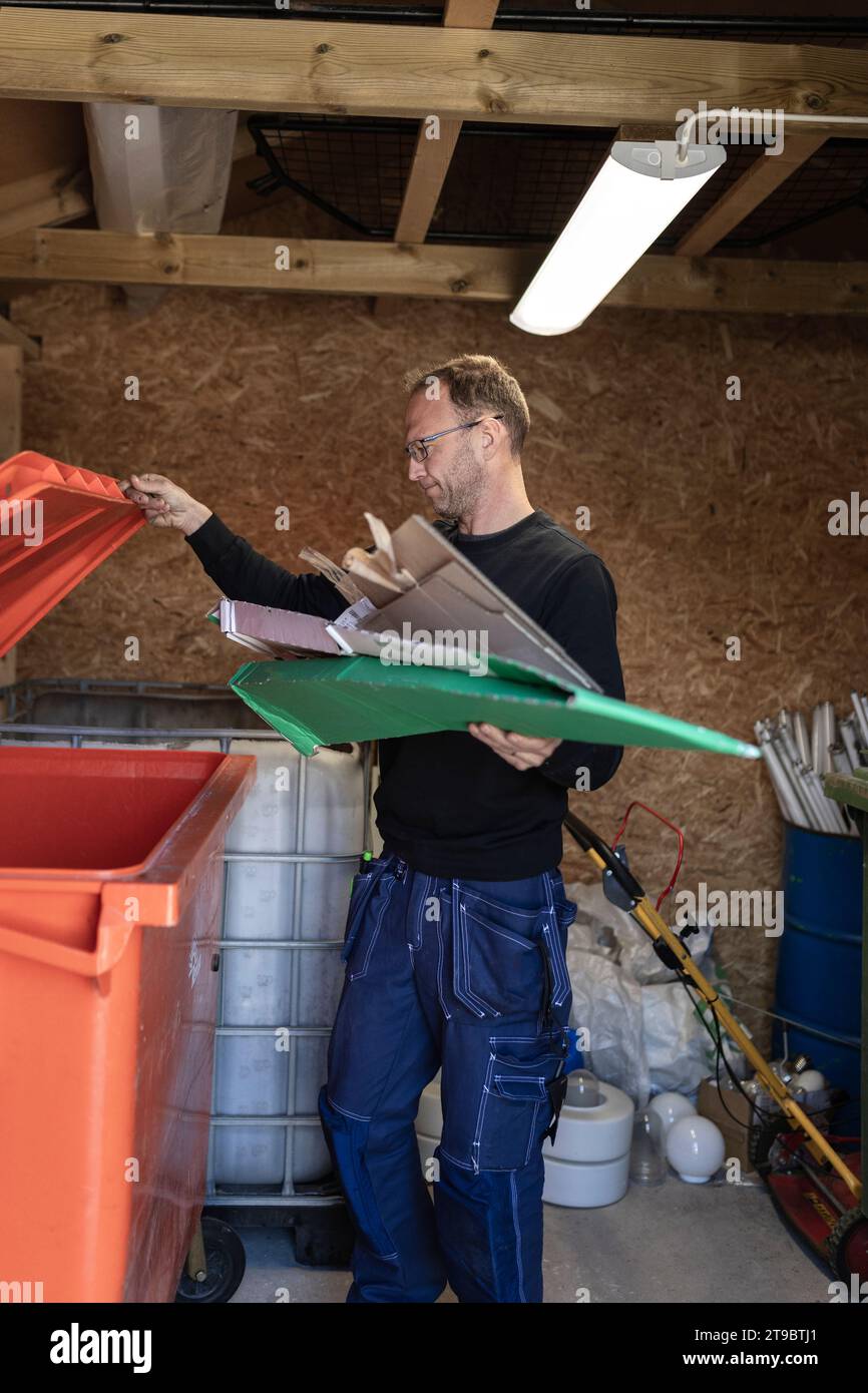 Männlicher Arbeiter, der Pappabfälle in Mülltonnen im Recyclingzentrum wirft Stockfoto