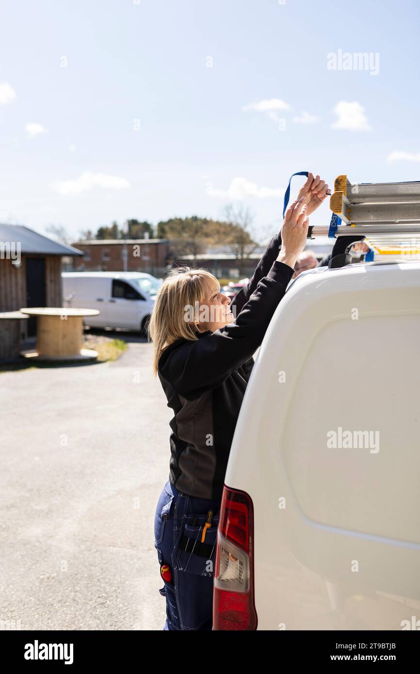 Frau, die an sonnigen Tagen im Stehen eine Leiter am Van bindet Stockfoto