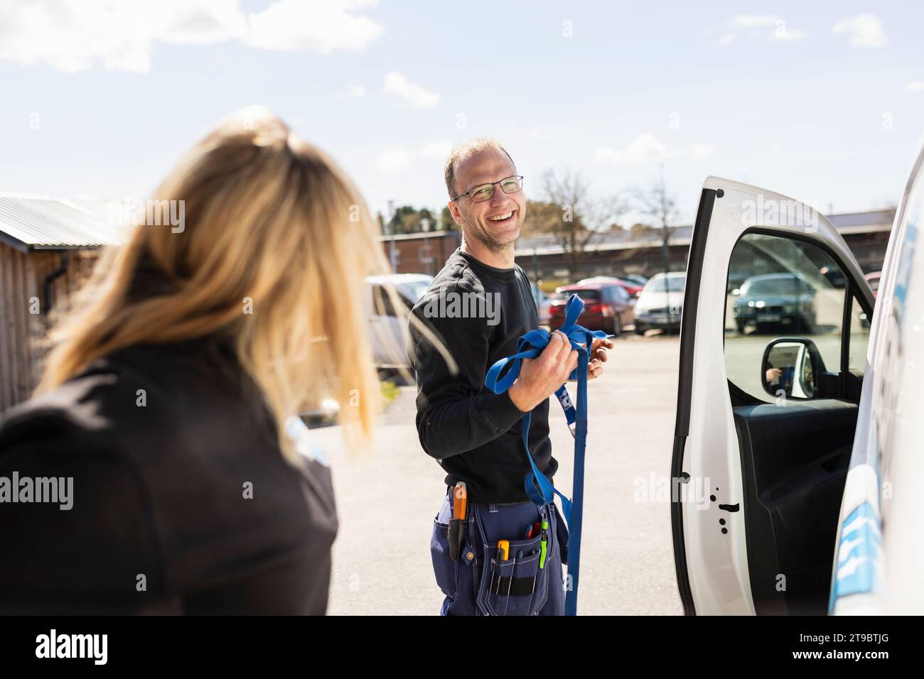 Glücklicher Elektriker, der mit einer Kollegin spricht, die an sonnigen Tagen am Van steht Stockfoto
