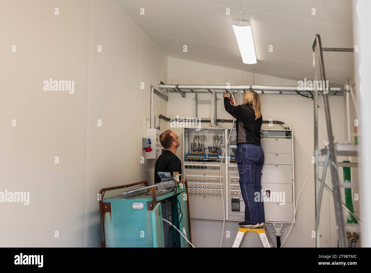 Elektrikerin, die Kabel im Messerraum neben einem Kollegen installiert Stockfoto